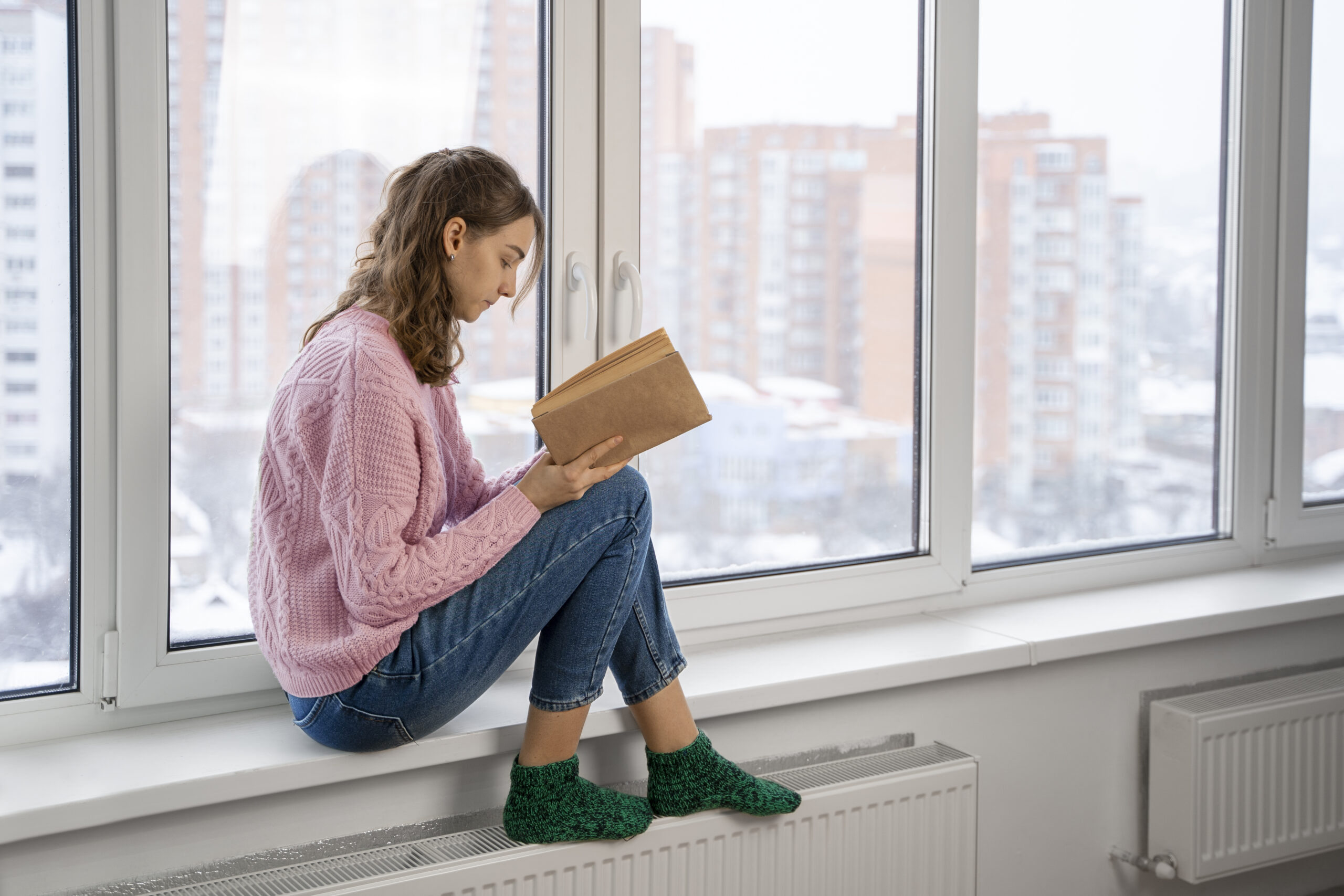 Девушка читает книгу на подоконнике у пластикового окна зимой