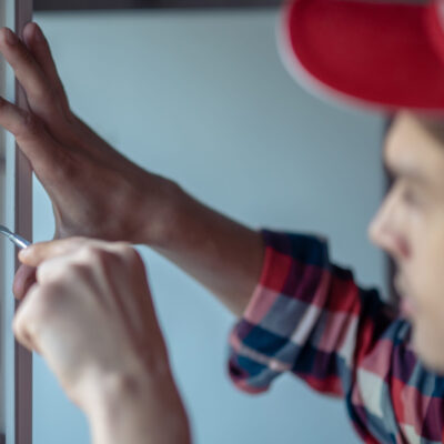 Мастер регулирует фурнитуру пластикового окна отверткой