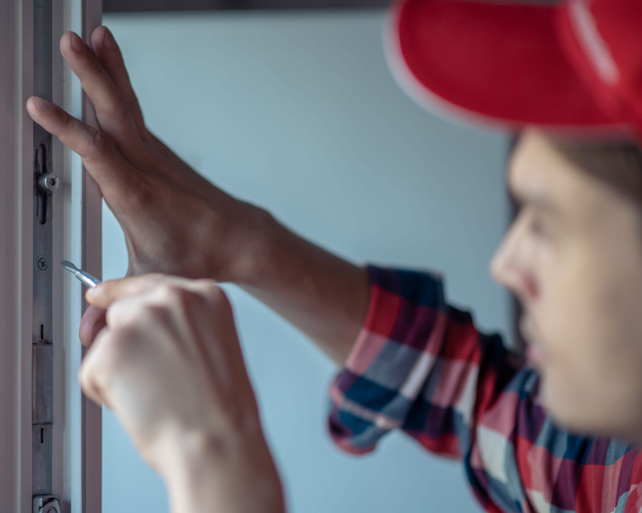 Мастер регулирует фурнитуру пластикового окна отверткой