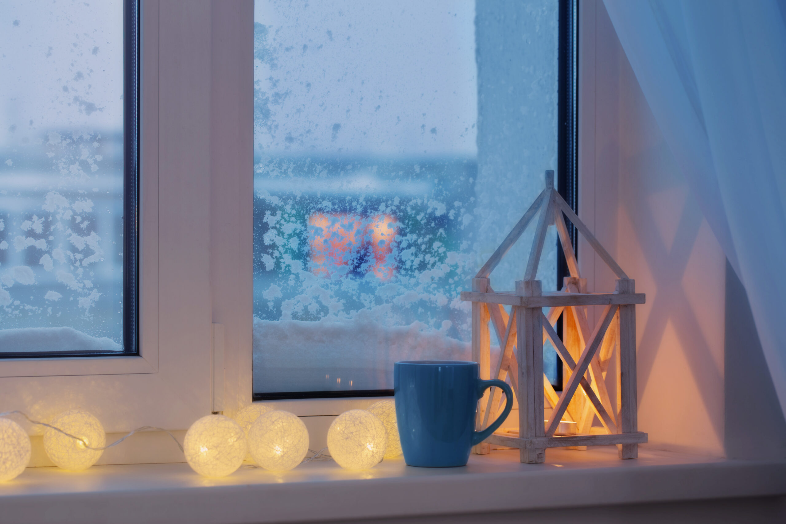 Заснеженное пластиковое окно зимой и декор на подоконнике